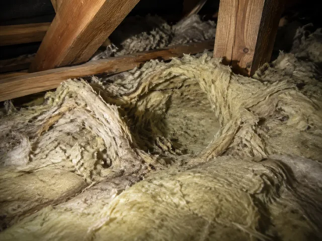 Aufgerissene und zu einer Mulde verdichtete Mineralwolldämmung in einem Dachstuhl